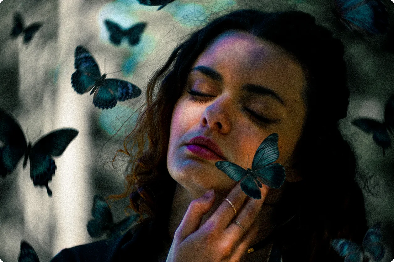 Eine Frau mit geschlossenen Augen hält einen Schmetterling an ihre Wange; um sie herum schweben dunkelblaue Schmetterlinge.