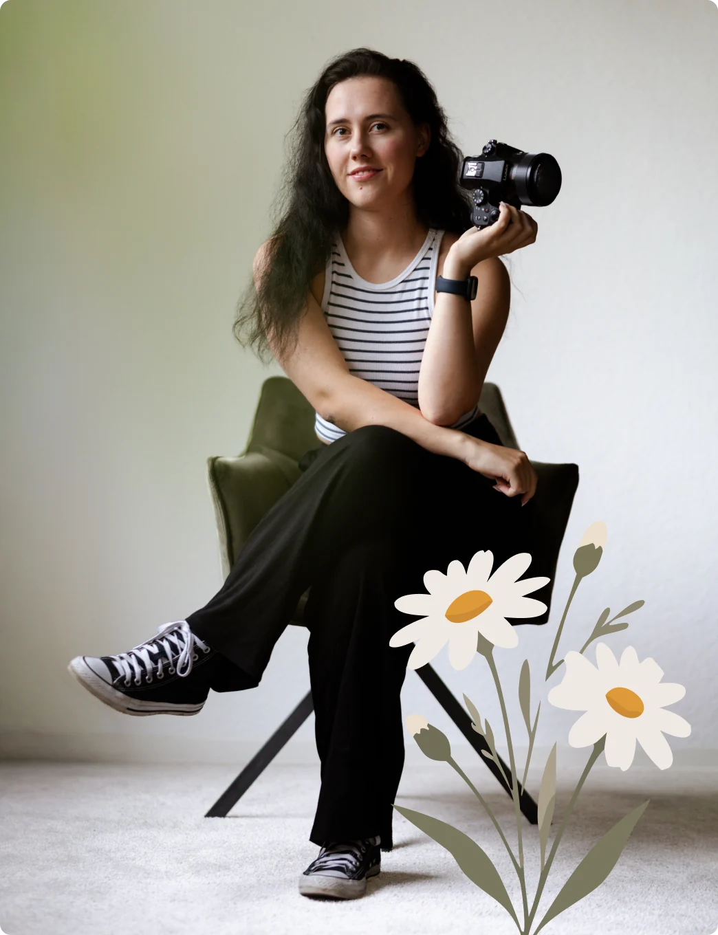 Die Fotografin sitzt mit überkreuzten Beinen auf einem olivgrünen Stuhl, hält ihre Kamera in der Hand und lächelt leicht; vorn rechts ragen illustrierte Gänseblümchen ins Bild.